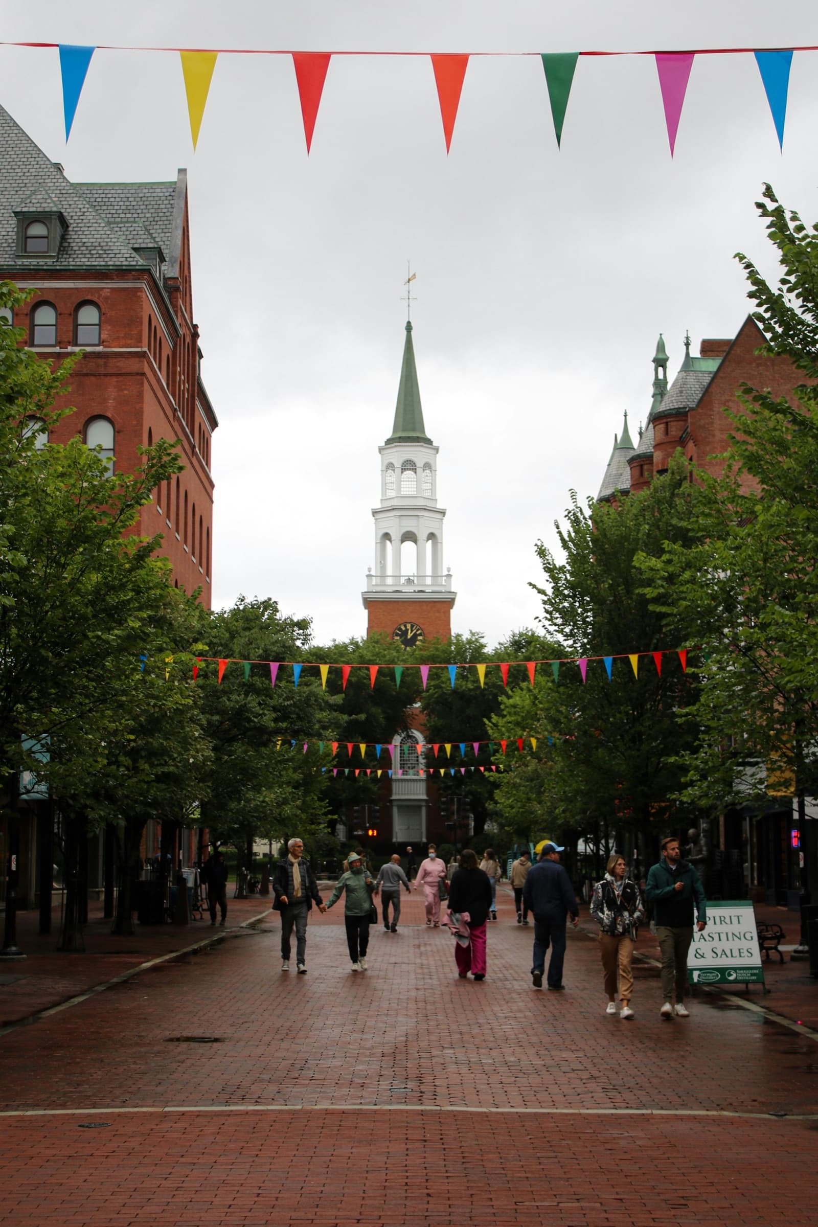 Church Street Marketplace in downtown Burlington on an overcast day, pennants strung between the brick buildings and people walking the street