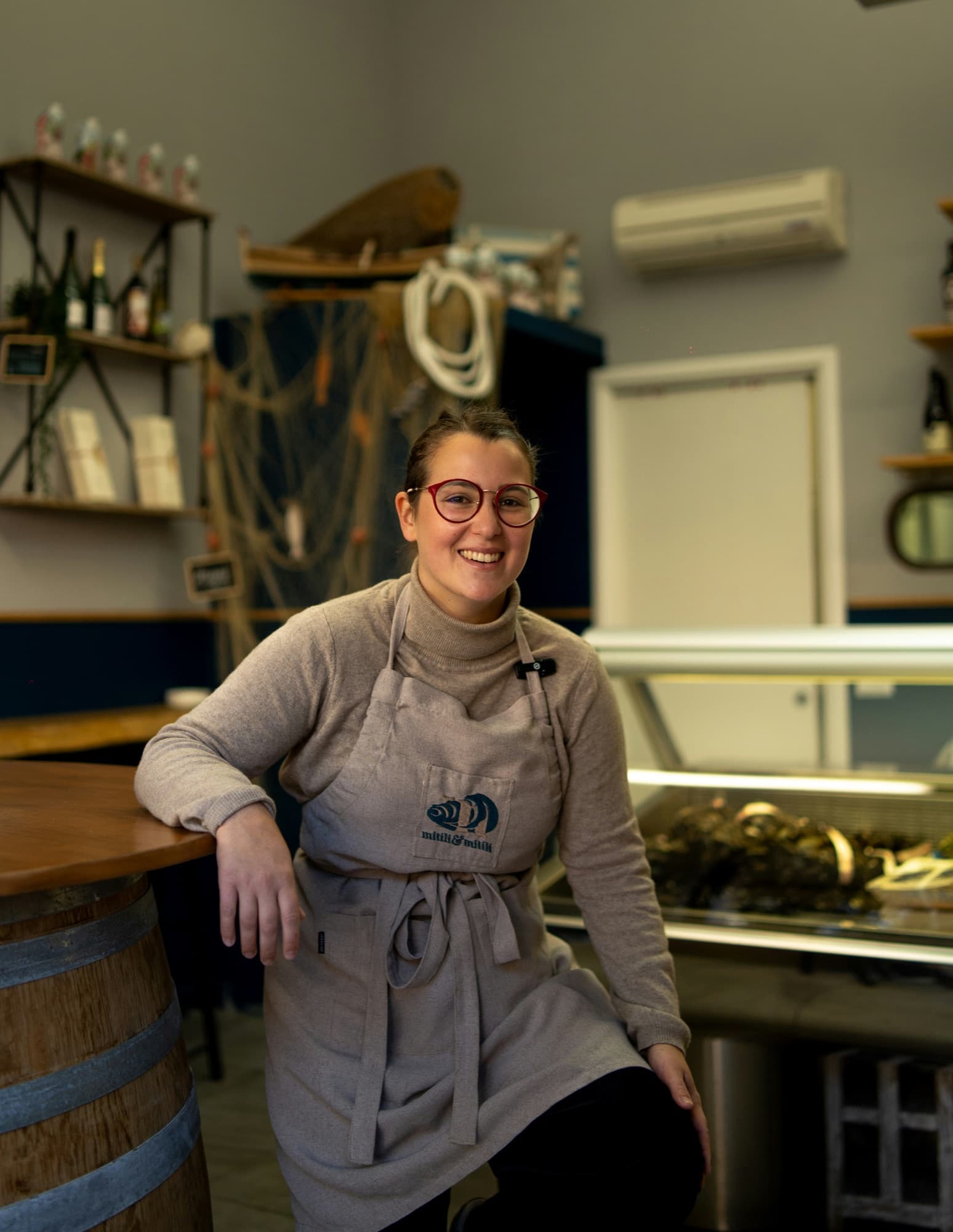 A shop owner in an apron smiling beside the counter of a small food shop